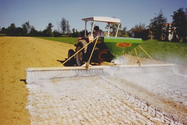 Трактор с разбрасывателем удобрений обрабатывает поле.